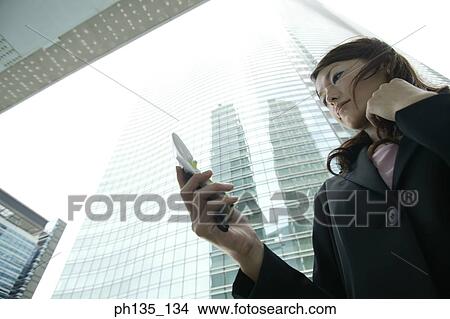 Low angle view of a young businesswoman operating a mobile phone View Large Photo Image Picture - Low angle view of a young businesswoman operating a mobile phone. Fotosearch