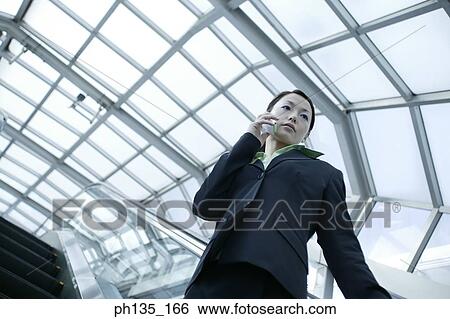 Young businesswoman standing on an escalator talking on a mobile phone View Large Photo Image Stock Photograph - Young businesswoman standing on an escalator talking on a mobile phone. Fotosearch
