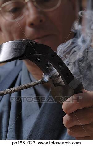 Stock Image - Close-up of a carpenter making holes on a wooden structure with a hot rod. Fotosearch