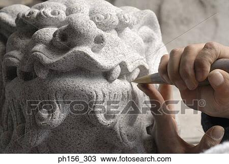 Stock Image - Close-up of a person's hand carving a statue with a chisel. Fotosearch