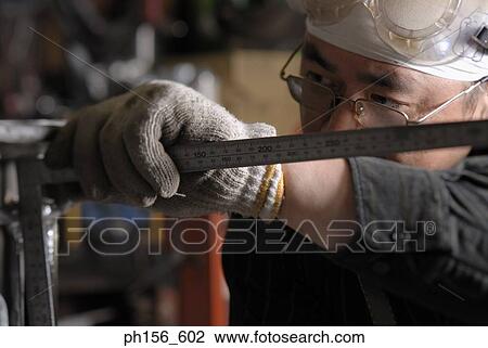 Stock Image - Close-up of a mid adult man measuring a metal rod in a workshop. Fotosearch