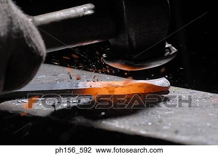 Stock Image - Close-up of a person's hand hitting molten metal with a hammer. Fotosearch