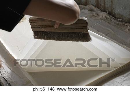 Stock Photo - Close-up of a person's hand holding a brush over sheets of paper. Fotosearch