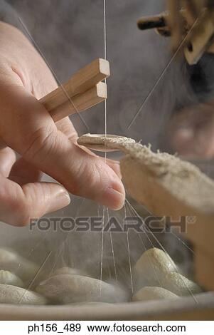 Stock Photo - Close-up of a person's hand pulling silk threads from silk cocoons. Fotosearch