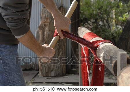 Stock Image - Mid section view of a man squeezing silk threads with a wooden stick. Fotosearch