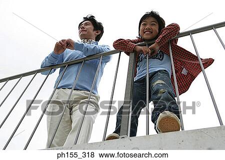 Stock Photo - Low angle view of a mid adult man and his son leaning against a railing. Fotosearch