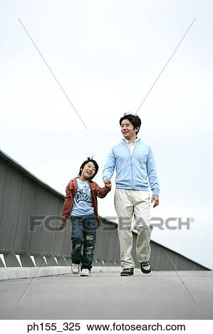 Stock Photography - Mid adult man walking on the road and holding his son's hand. Fotosearch