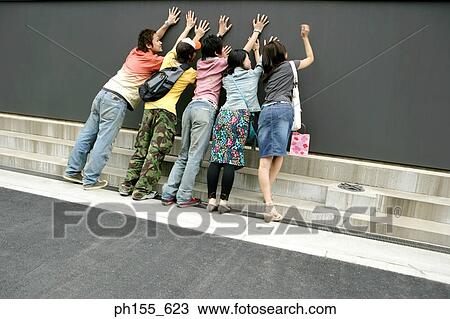 Rear view of two young women and three men leaning over a wall View Large Photo Image Stock Image - Rear view of two young women and three men leaning over a wall. Fotosearch