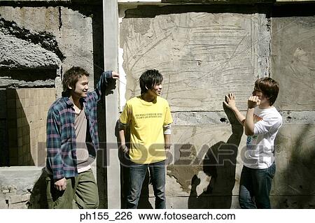 Three young men standing in front of wall View Large Photo Image Stock Photograph - Three young men standing in front of wall. Fotosearch
