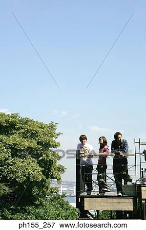Two young men and a young woman standing on a footbridge View Large Photo Image Stock Photo - Two young men and a young woman standing on a footbridge. Fotosearch
