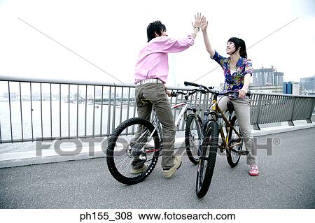 Stock Photo - Two young men sitting on a bicycle and giving high-five. Fotosearch