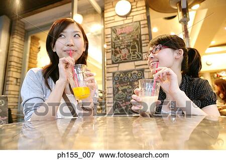 Two young women sitting together and sipping juice View Large Photo Image Stock Photo - Two young women sitting together and sipping juice. Fotosearch