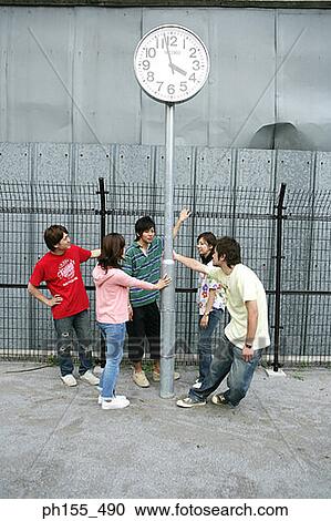 Stock Image - Five friends standing around a pole with a clock. Fotosearch