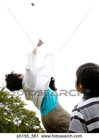 Low angle view of a father throwing a ball up with his son beside him View Large Photo Image Stock Image - Low angle view of a father throwing a ball up with his son beside him. Fotosearch