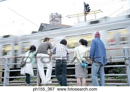 Stock Photo - Rear view of three men and two women leaning against a railing. Fotosearch