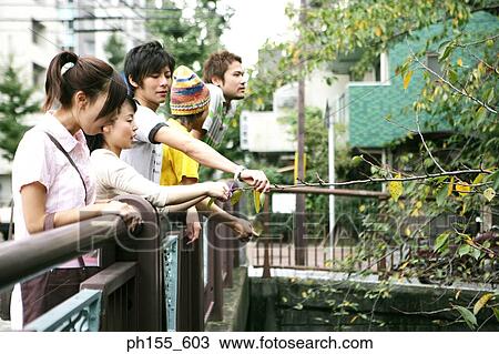 Stock Image - Two young women and three young men leaning over a railing. Fotosearch