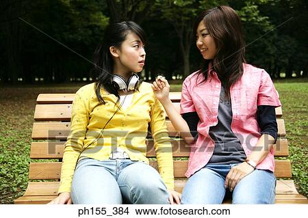 Two young women sitting on a park bench View Large Photo Image Picture - Two young women sitting on a park bench. Fotosearch
