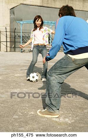 Stock Photography - Young woman playing football with a young man. Fotosearch