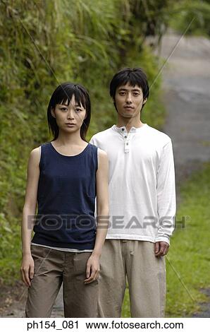Stock Image - Portrait of a young couple standing in a garden. Fotosearch
