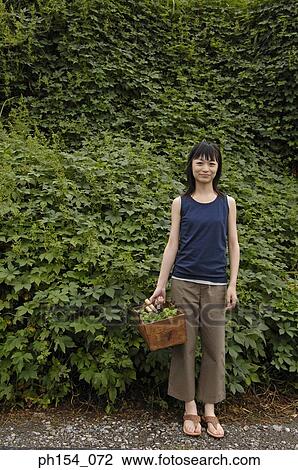 Portrait of a young woman holding a basket and standing in a garden View Large Photo Image Stock Image - Portrait of a young woman holding a basket and standing in a garden. Fotosearch
