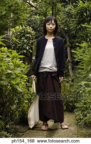 Portrait of a young woman standing in a garden View Large Photo Image Stock Photo - Portrait of a young woman standing in a garden. Fotosearch