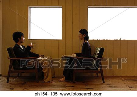 Stock Photography - Side profile of a young couple sitting near windows. Fotosearch