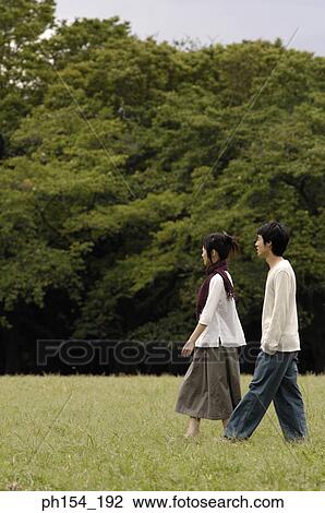 Stock Image - Side profile of a young couple walking together. Fotosearch