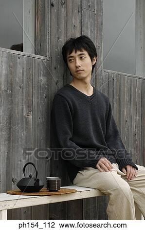 Stock Image - Side profile of a young man sitting on a bench. Fotosearch