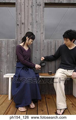 Stock Photograph - Young couple sitting on a bench and having tea. Fotosearch