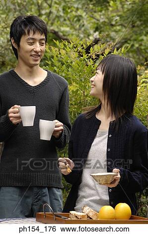 Young woman holding a bowl and a fork with a young man standing behind her holding coffee cups View Large Photo Image Stock Photograph - Young woman holding a bowl and a fork with a young man standing behind her holding coffee cups. Fotosearch