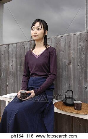 Stock Photograph - Young woman holding a cup and sitting on a bench. Fotosearch