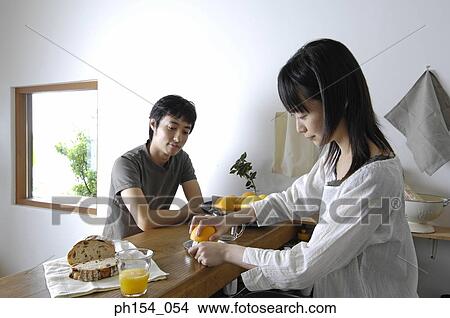 Young woman squeezing an orange in a juicer with a young man sitting in front of her View Large Photo Image Picture - Young woman squeezing an orange in a juicer with a young man sitting in front of her. Fotosearch