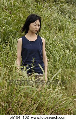 Stock Image - Young woman standing on a field. Fotosearch