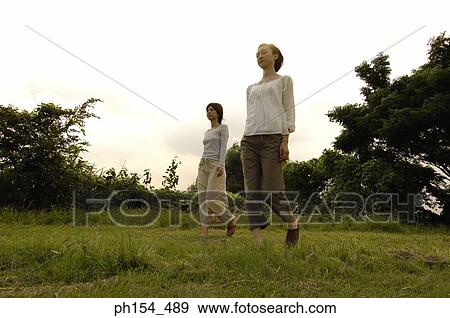 Low angle view of two young women walking in a field View Large Photo Image Stock Photo - Low angle view of two young women walking in a field. Fotosearch