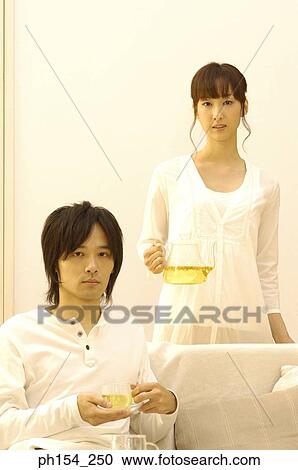 Portrait of a young man holding a cup of tea with a young woman holding a teapot behind him View Large Photo Image Stock Image - Portrait of a young man holding a cup of tea with a young woman holding a teapot behind him. Fotosearch
