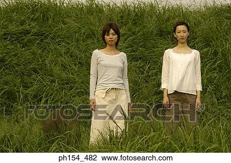 Portrait of two young women standing in a field View Large Photo Image Stock Image - Portrait of two young women standing in a field. Fotosearch