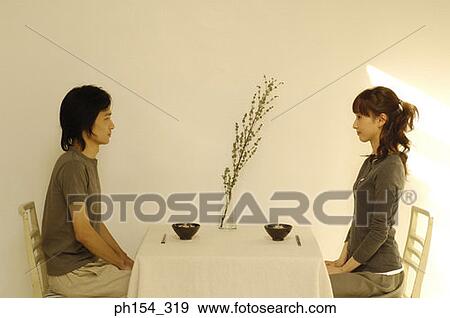 Side profile of a young couple sitting at the dining table View Large Photo Image Stock Photo - Side profile of a young couple sitting at the dining table. Fotosearch