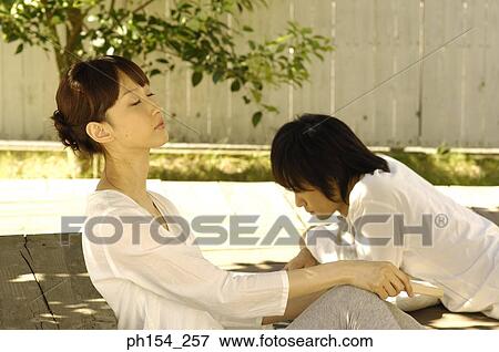 Side profile of a young woman leaning against a bench with a young man lying beside her View Large Photo Image Stock Photo - Side profile of a young woman leaning against a bench with a young man lying beside her. Fotosearch