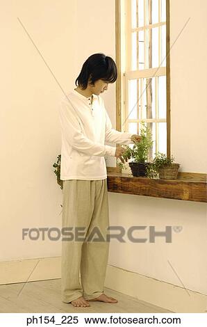 Stock Photography - Young man watering a potted plant. Fotosearch