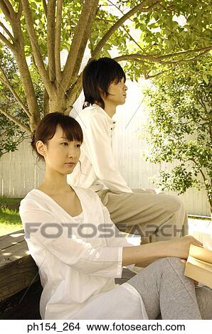 Picture - Young woman holding a book with a young man sitting on the bench. Fotosearch