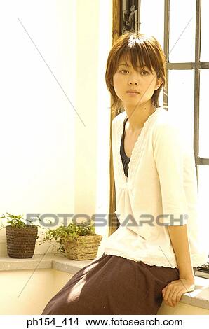 Young woman sitting on a window sill and looking away View Large Photo Image Picture - Young woman sitting on a window sill and looking away. Fotosearch