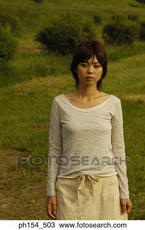 Young woman standing in a field View Large Photo Image Stock Image - Young woman standing in a field. Fotosearch