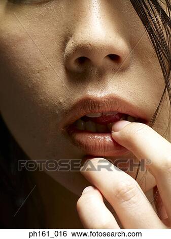Stock Photograph - Young woman with finger to her mouth, close-up. Fotosearch