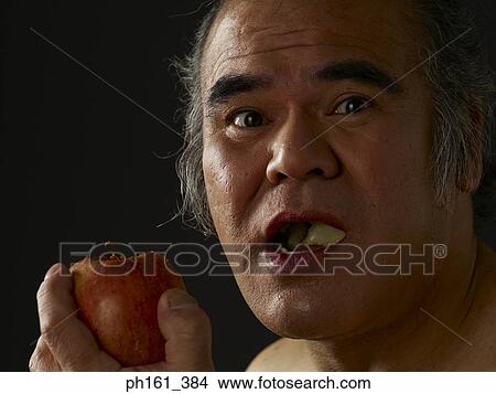 Picture - Mature man holding an apple with his mouth open. Fotosearch