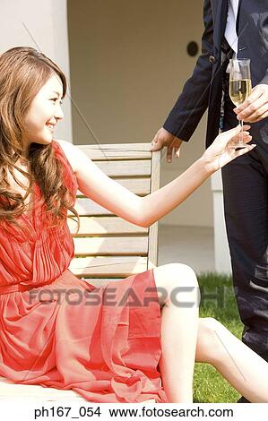 Picture - A young man handing a glass of champagne to a woman. Fotosearch