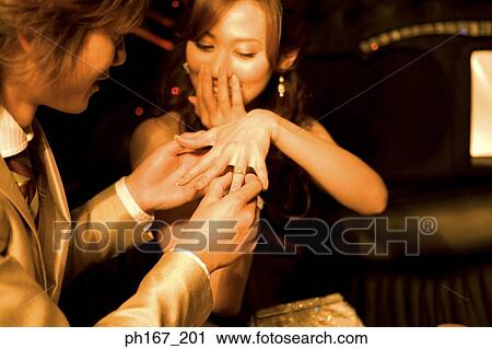 Young man placing ring on woman's finger View Large Photo Image Stock Image - Young man placing ring on woman's finger. Fotosearch