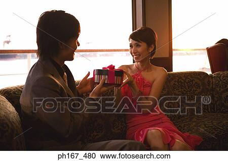 Stock Image - Couple sitting on couch, holding a gift. Fotosearch