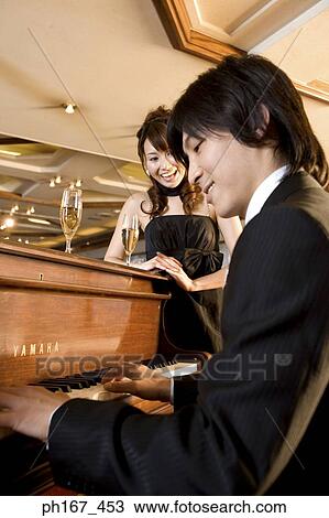 Stock Image - Woman looking at man playing piano. Fotosearch