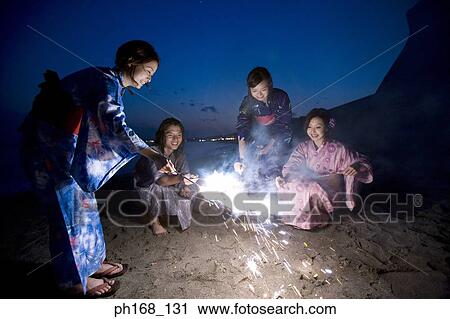 Stock Image - A small group of people with sparklers at the beach. Fotosearch