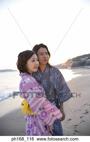 Couple standing by the beach, sunset View Large Photo Image Stock Photograph - Couple standing by the beach, sunset. Fotosearch